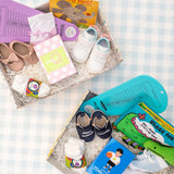 A collection of baby items neatly arranged in two boxes, including socks, shoes, a storybook, and other baby essentials.