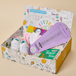 A baby foot gift box in a decorative cardboard box, featuring a purple measuring tool, white and blue baby shoes, pink socks, a colorful book, and a green 'The Foot Book' on a beige background.
